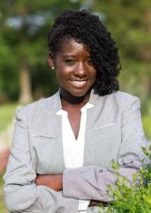 Headshot of Abenaa Jones with medium long curly dark hair in gray blazer.