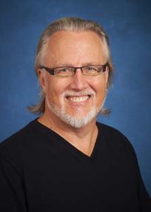 Headshot of David Baker with thin-rimmed glasses wearing a black shirt.