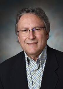 White male, grey hair, glasses, smiling, wearing a collared plaid shirt.