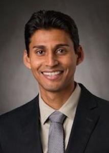 Vikash Gayah Headshot, with short black hair, tan shirt, tie, and black jacket.