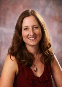 Headshot of Kristin Buss with long brown hair, silver necklace, and maroon top.
