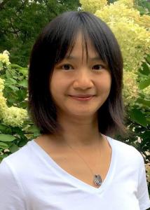 Headshot of Liying Luo outside with mid-length, dark hair and wearing a necklace and white v-neck.