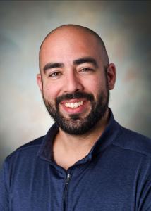 Headshot of Dr. Nelson Roque with bald head, black beard, and dark blue shirt..