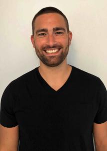 Ryan Thomas headshot with short black hair, beard, and black shirt smiling.