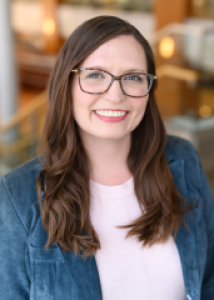 Headshot of Jessica Thompson, a young white woman with brown glasses and long brown hair wearing a blue jacket.